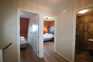A hotel room with a bed, a bathroom with a shower, and a hallway leading to another room. - Brand new Corner Villa in Friesland (Leons)