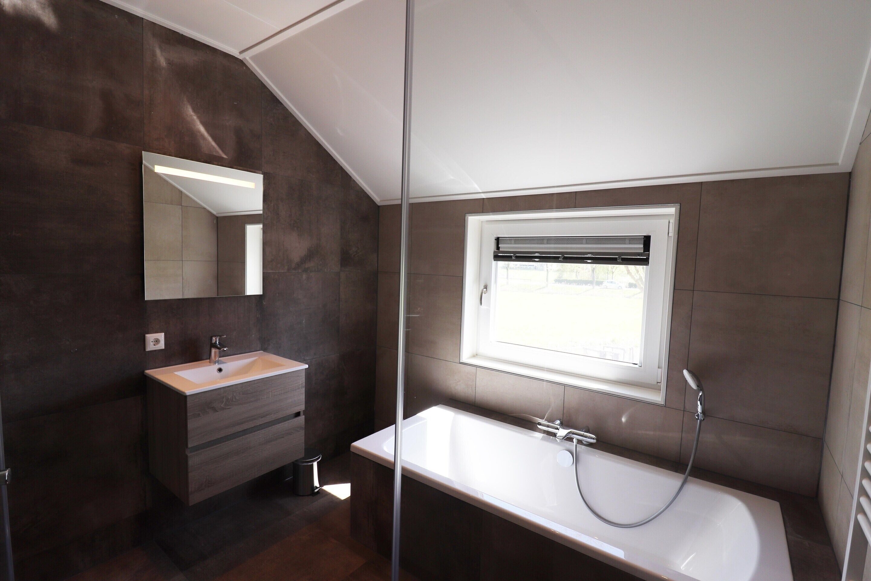 A modern bathroom with a large mirror, a bathtub, and a window.