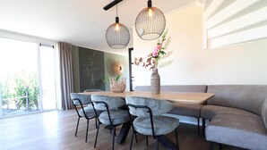 Un espace de salle à manger moderne avec une table en bois, des chaises à revêtement gris et deux lampes suspendues.