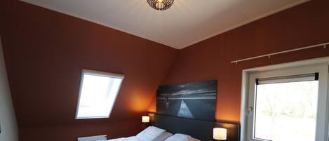 A bedroom with a bed, two bedside tables, two wall-mounted lamps, and two windows.