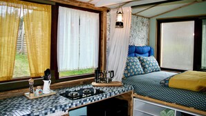 A compact room with a kitchenette, a bed with patterned bedding, and a window with curtains.