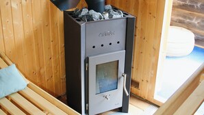 A wood-burning stove in a cabin with a bed and a window.