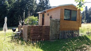 Une petite cabane en bois avec une seule fenêtre, une porte et un espace clos comprenant un banc et un barbecue.