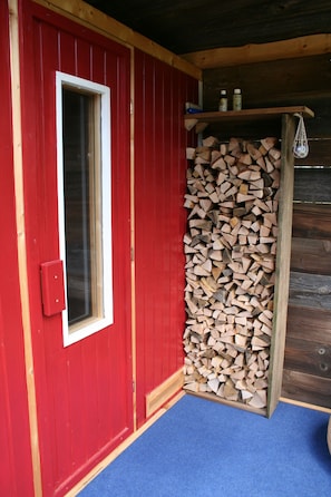 A red door with a window, a stack of firewood, and a blue carpet.