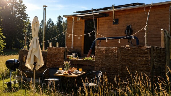 Un chalet rustique en bois, doté d’un coin repas, d’un barbecue extérieur et de guirlandes lumineuses.
