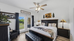 A bedroom with a bed, a ceiling fan, a nightstand, a bench, a window with blinds, and a wall-mounted artwork. - Poolside Bear Escape Indoor and Outdoor Fun (Pigeon Forge)