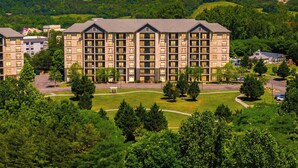 Een hotel met meerdere verdiepingen en een centrale binnentuin, omringd door weelderige begroeiing en heuvels op de achtergrond.