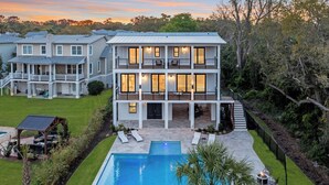 Une maison à deux étages avec une piscine, un espace salon extérieur et une terrasse couverte.