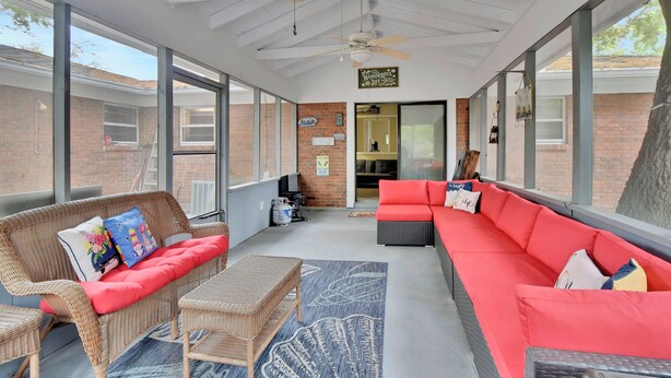 Un patio couvert aménagé avec des meubles en osier, un canapé rouge et un ventilateur de plafond.