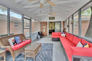 Un patio cubierto con mobiliario de mimbre, un sofá rojo y un ventilador de techo.
