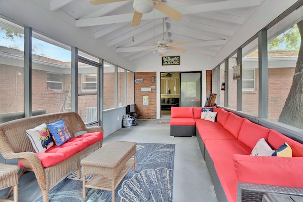A covered patio area with wicker furniture, a red sofa, and a ceiling fan. - Comfortable 3 bedroom/2 bath house close to the pier/village area (Saint Simons Island)