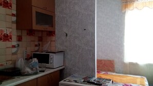 A small kitchen with a microwave, a small table with magazines, and a bed with a floral bedspread.
