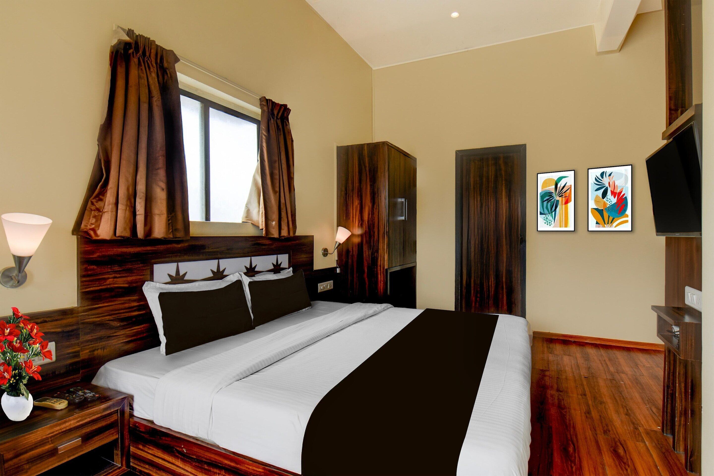 A hotel room with a large bed, wooden headboard, two bedside tables, a nightstand, a lamp, a TV, and artwork on the wall.