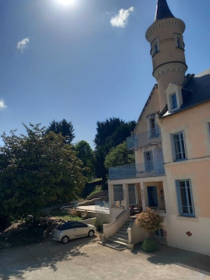 A two-story building with a tower, a car parked in front, and a staircase leading to the entrance. - Lovely gîte in an exceptional setting (Dangé-Saint-Romain)