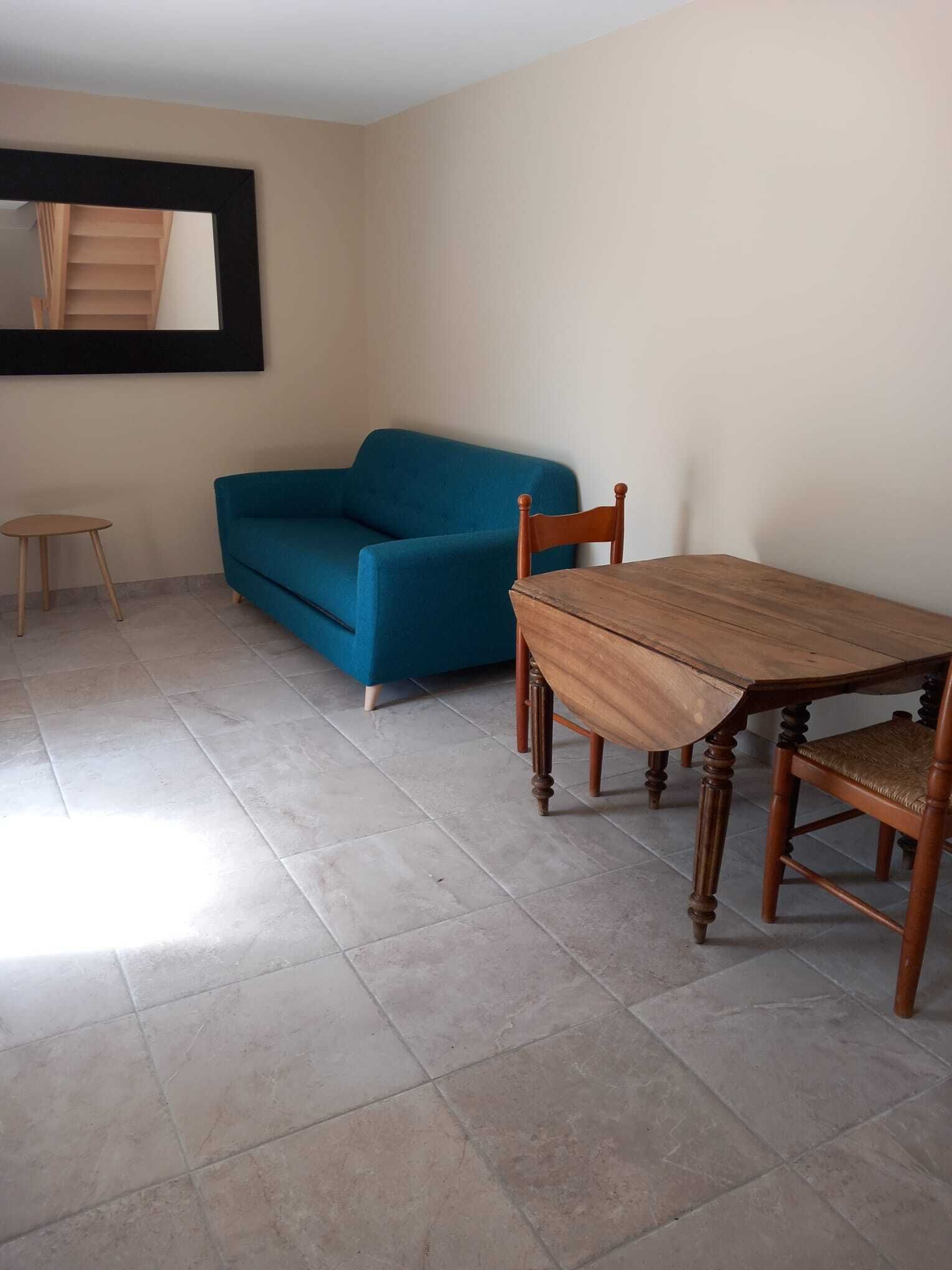 A room with a wooden dining table, a blue sofa, and a small wooden stool.