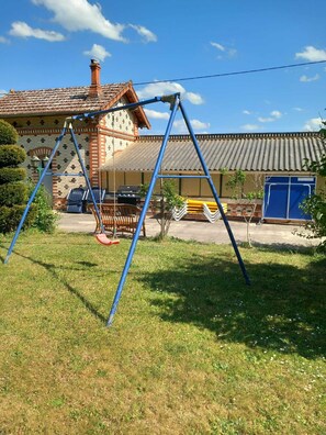 A residential area with a brick house, a swing set, and a blue door. - Lovely gîte in an exceptional setting (Dangé-Saint-Romain)