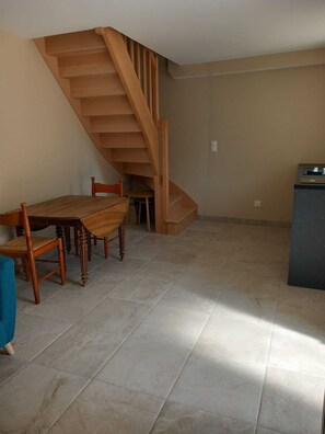 A dining area with a wooden table and chairs, a staircase, and a tiled floor. - Lovely gîte in an exceptional setting (Dangé-Saint-Romain)