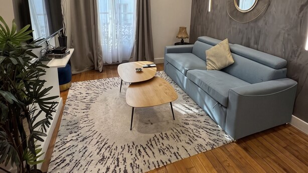 Ein modernes Wohnzimmer mit einem blauen Sofa, einem Flachbildfernseher, einer Kristallleuchtre und einem großen Spiegel an der Wand.