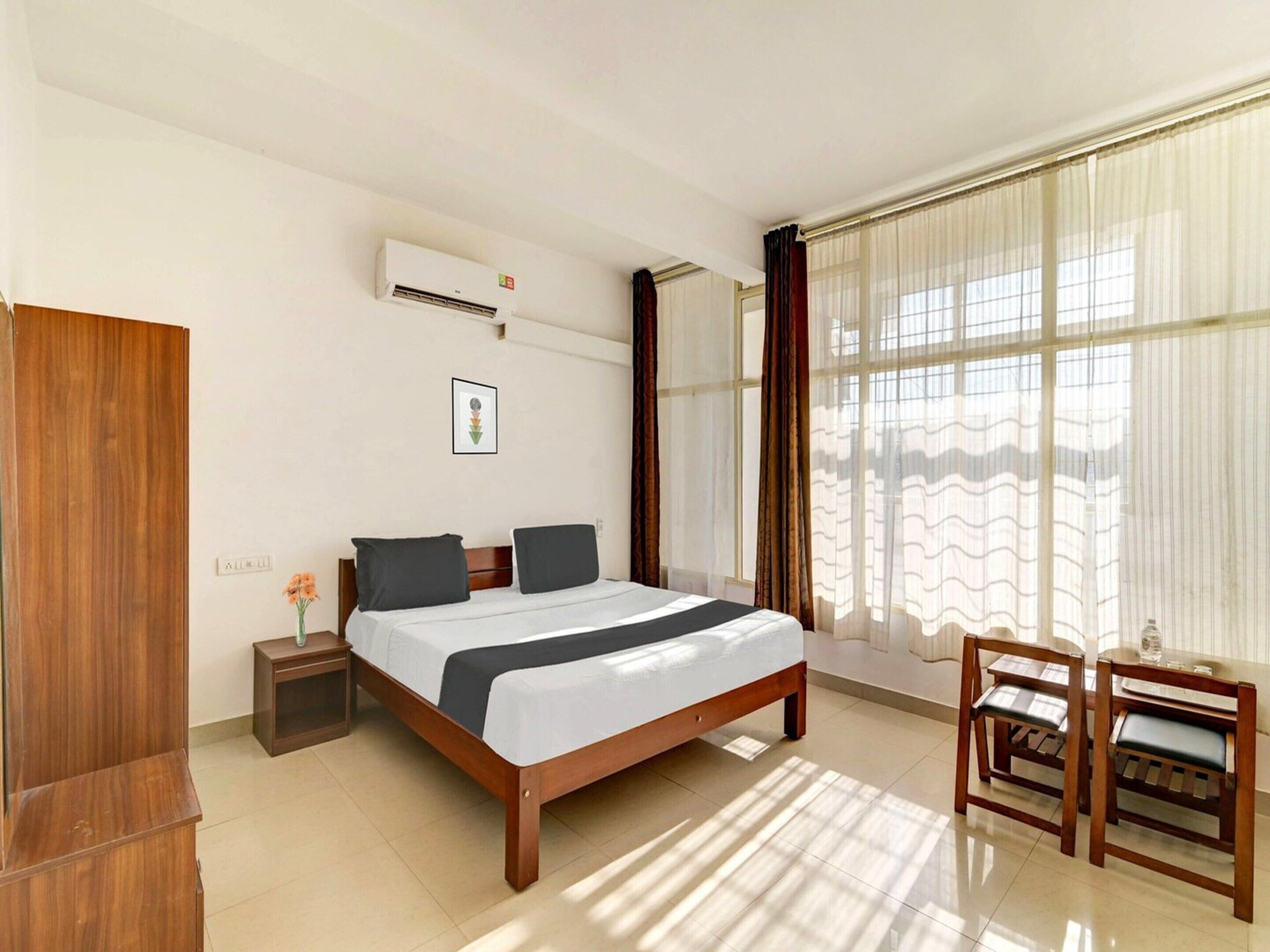 A bedroom with a bed, bedside table, chair, and window with curtains.