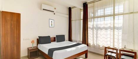 A bedroom with a bed, bedside table, chair, and window with curtains.