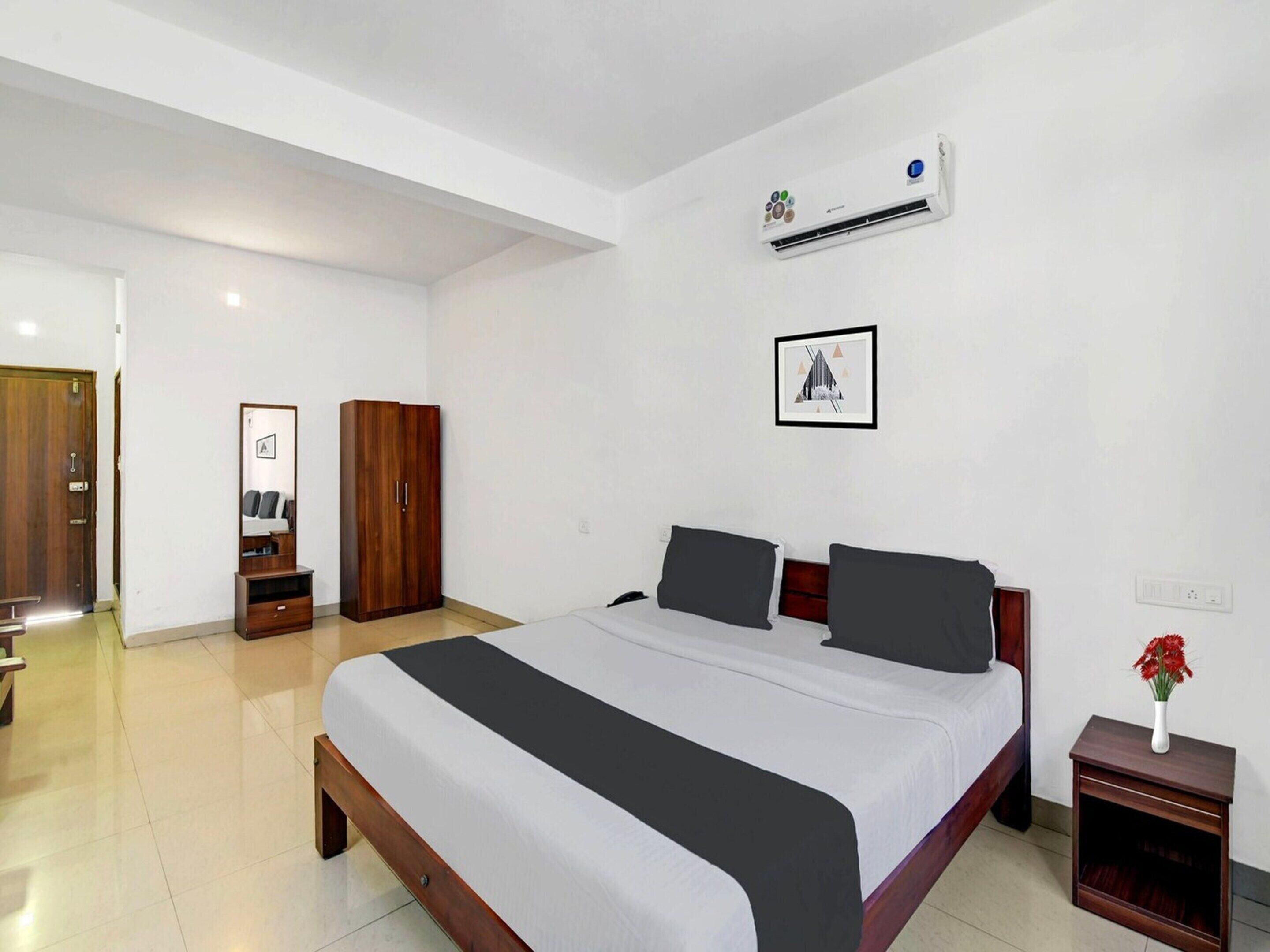 A bedroom with a bed, a wardrobe, a mirror, an air conditioning unit, and a framed picture on the wall.