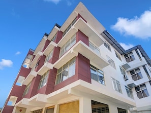 A multi-story building with a modern architectural design, featuring a combination of white and maroon colors, large windows, and a visible garage door.