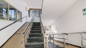 A staircase with metal railings, a fire exit sign, and large windows. - Classic With Balcony Madikeri (Madikeri)