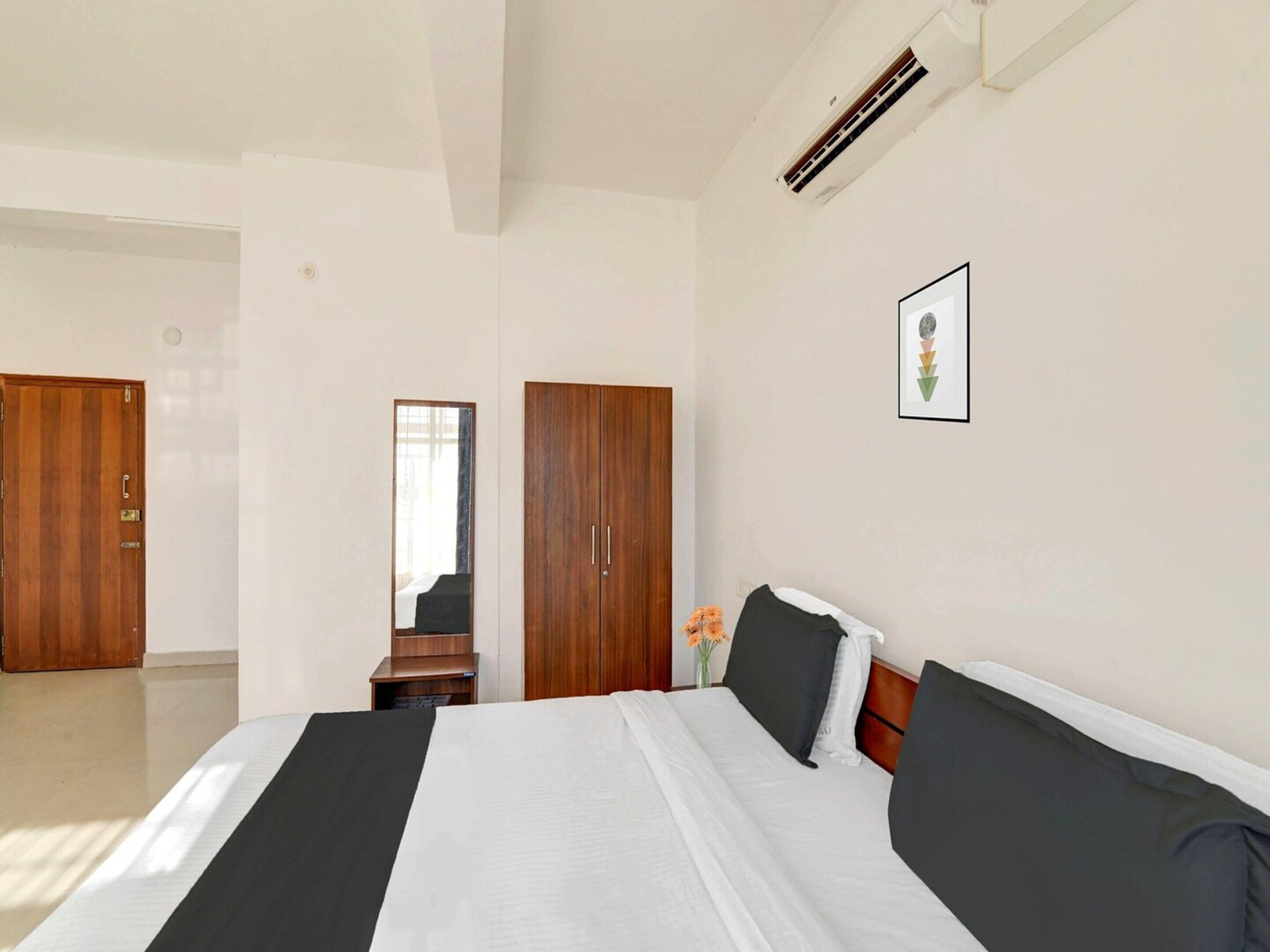 A hotel room with a bed, a wardrobe, a mirror, and a framed picture on the wall.