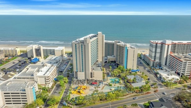 Ett hotellkomplex vid kusten med flera höga byggnader, en parkeringsplats och utsikt över stranden.