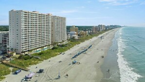Ein Strandhotel mit mehreren Etagen, einem Sandstrand und freiem Blick auf den Ozean.