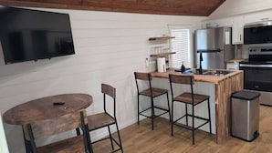 Una cocina compacta con una mesa de madera, taburetes de bar, un televisor montado en la pared y electrodomésticos modernos.