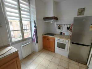 Eine Küche mit Fenster, Herd, Backofen, Kühlschrank und Fliesenboden.