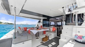 L'intérieur d'un bateau, avec un coin repas, des sièges et une vue sur la mer.