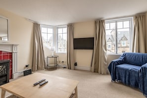 A hotel room with a sofa, a TV, a fireplace, and a view of buildings outside.