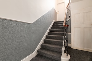A staircase with a patterned wall, a white door, and a handrail.