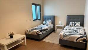 A bedroom with two beds, a bedside table, a nightstand, a window, and a potted plant. - Modern Beachfront 2BR with Terrace, A/C, WiFi & Garage in top location (Quarteira)