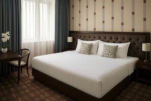 A hotel room with a large bed, a desk, two chairs, a potted plant, and a nightstand with a lamp. - Yerevan Resident (Yerevan)