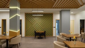 A modern interior with a geometric wall design, wooden ceiling beams, and a dining area with tables and chairs.