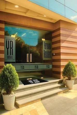 A hotel entrance with a glass facade, steps leading up to the door, and potted plants. - Yerevan Resident (Yerevan)