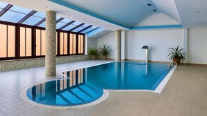 An indoor swimming pool with a skylight, tiled floor, and potted plants.