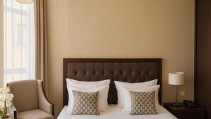 A hotel room with a large bed, two pillows, a chair, a nightstand, a lamp, and a window with curtains.