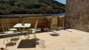 Une terrasse avec une table et des chaises, un mur en pierre et une vue sur un lac et une forêt.
