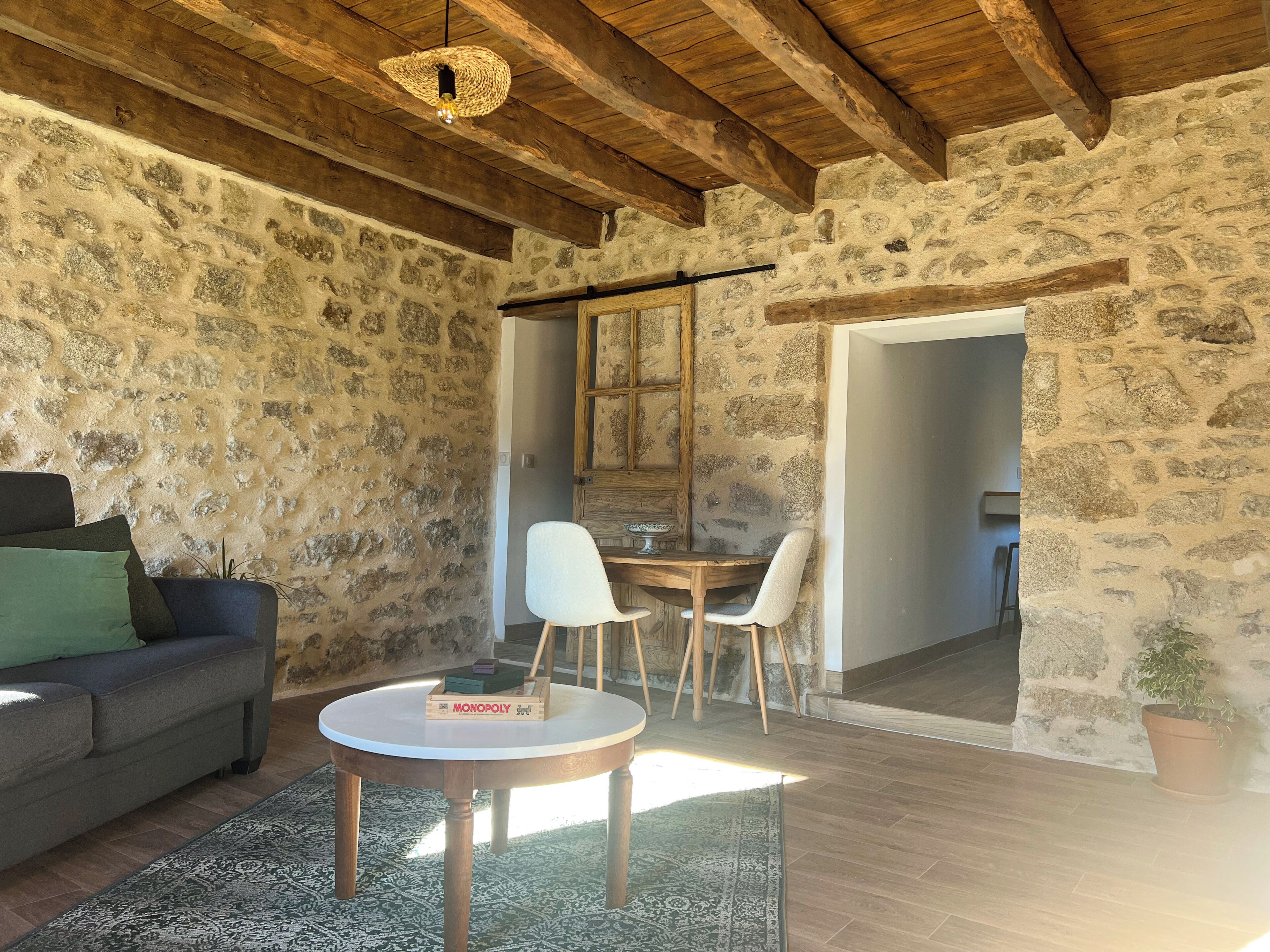 Um quarto rústico com paredes de pedra, teto de madeira, uma mesa redonda com cadeiras, um sofá e um jogo de Banco Imobiliário.