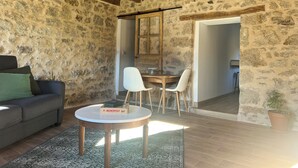 Une pièce rustique avec des murs en pierre, un plafond en bois, une table ronde entourée de chaises, un canapé et un jeu de société Monopoly.