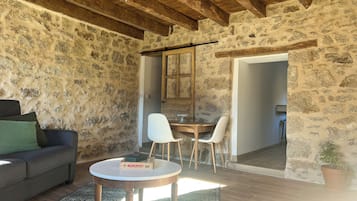 Um quarto rústico com paredes de pedra, teto de madeira, uma mesa redonda com cadeiras, um sofá e um jogo de Banco Imobiliário.