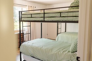 Una cama litera con ropa de cama verde y blanca a rayas, una ventana con cortinas y un armario de madera.