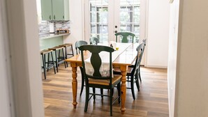 Een eetgedeelte met een houten tafel en stoelen, een keuken op de achtergrond en een kroonluchter.