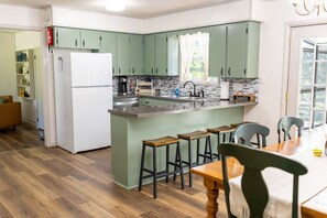 A kitchen with a refrigerator, a sink, and a dining area with stools.