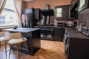 Eine moderne Küche mit einer zentralen Kochinsel, Barhocker, einem eingebauten Backofen und einem großen Fenster.