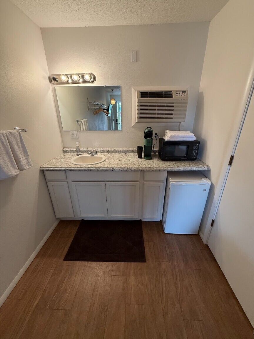 A compact bathroom with a sink, vanity, mirror, and a microwave.